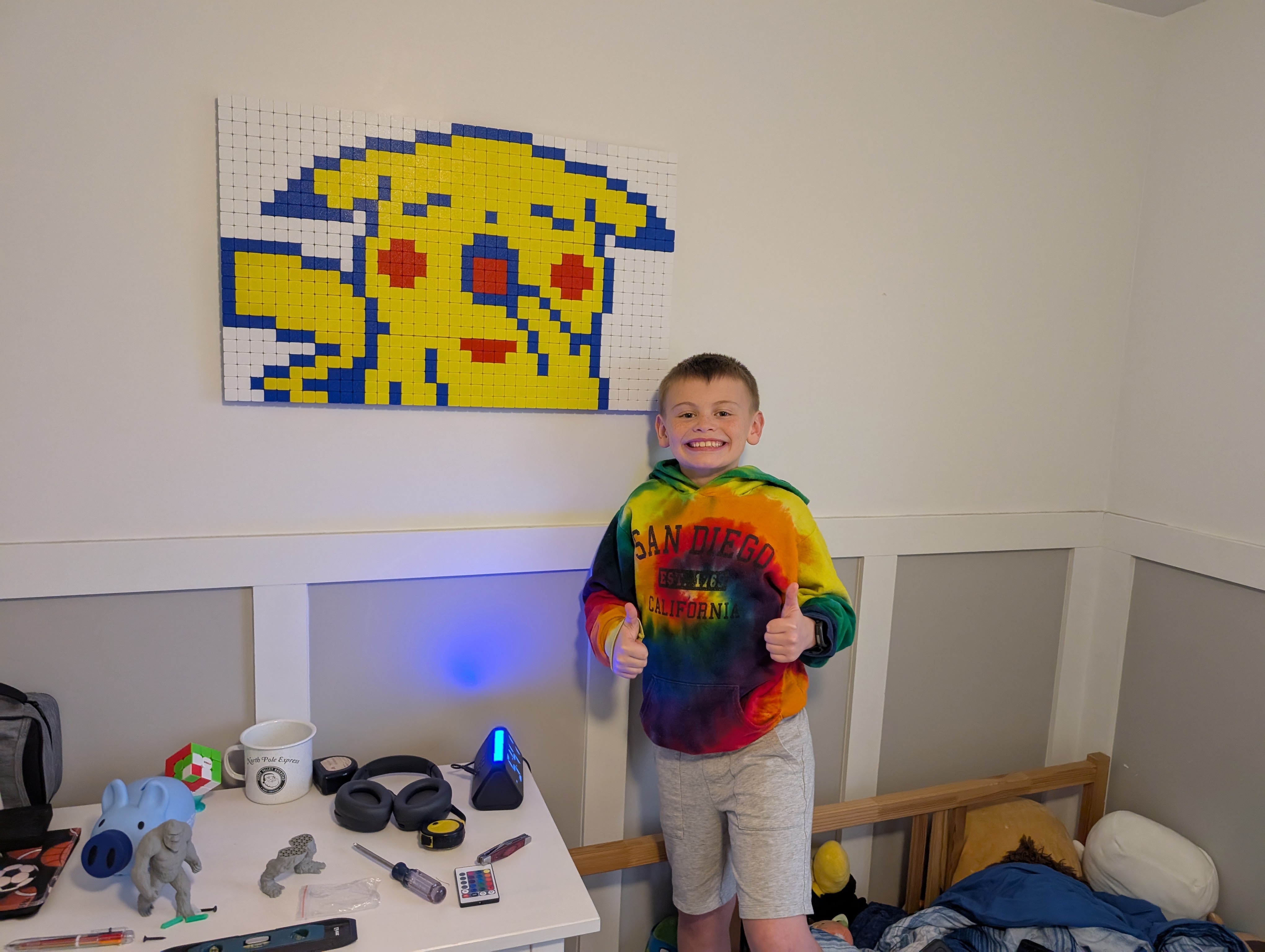 A smiling child beside a finished Klixel character mounted on the wall